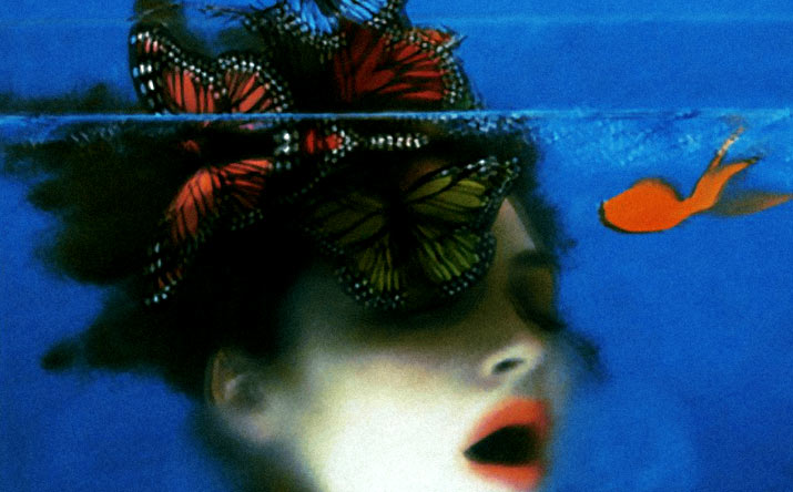 Inspiration friday post of Sarah Moon Photo of a girl with pale skin and bright red lips with her mouth open under water with butterflies in her hair
